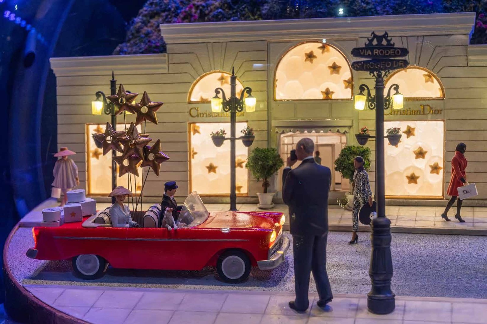 Miniature street diorama with a red car and lit storefront at night.
