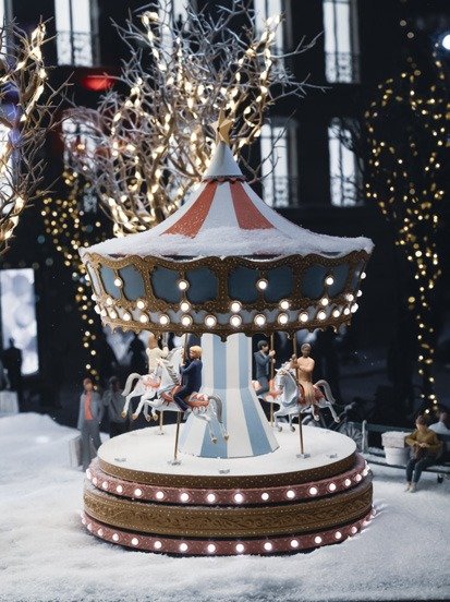 Miniature carousel model on artificial snow with bare lit branches behind.