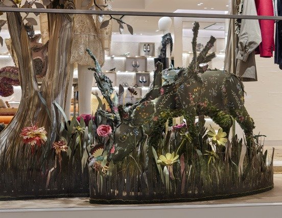 Close-up of a floral-covered fawn sculpture in a grass-and-flower window scene.