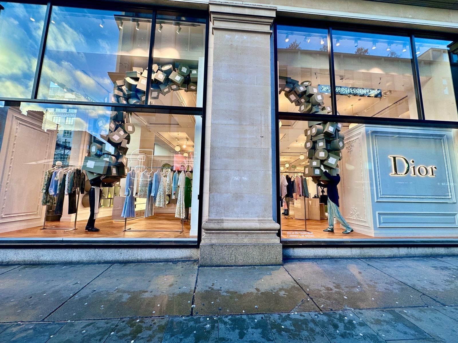 Boutique storefront windows with cascading grey box installations behind glass at dusk.