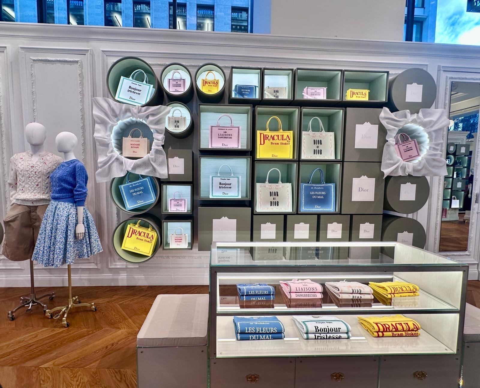 Wall display of grey compartments holding printed tote bags above a folded-scarf case.