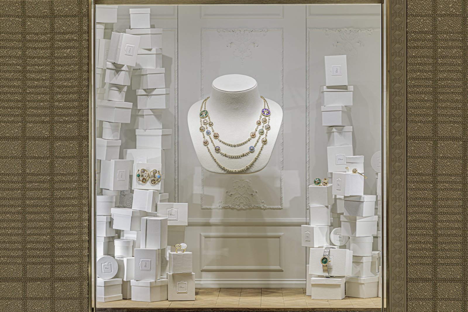 Window with a beaded necklace on a bust framed by stacks of white boxes.