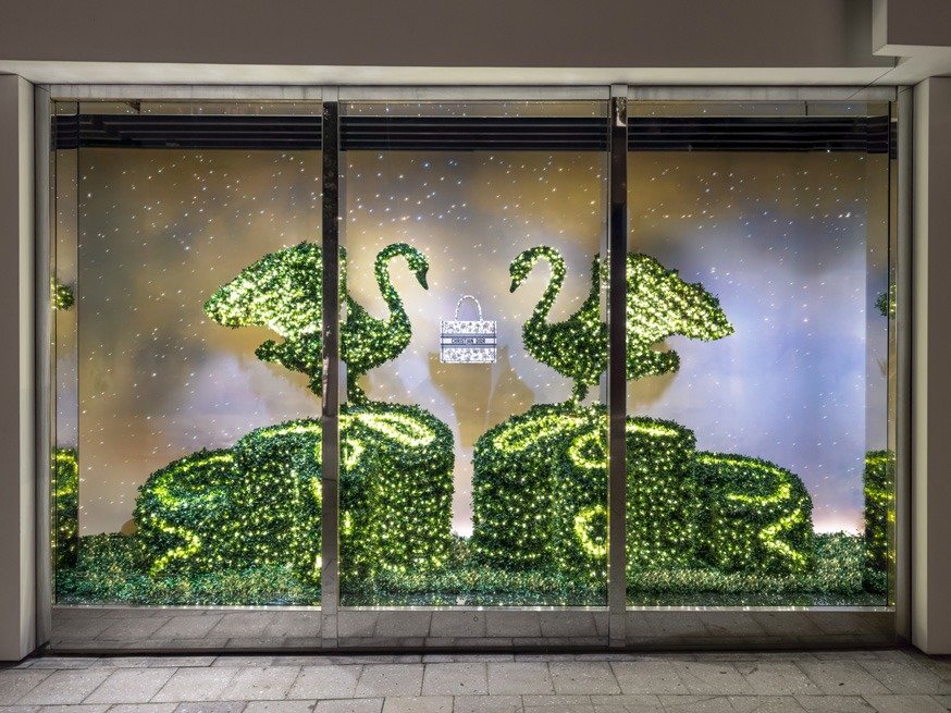 Illuminated swan topiaries flanking a small handbag in a lit storefront window.