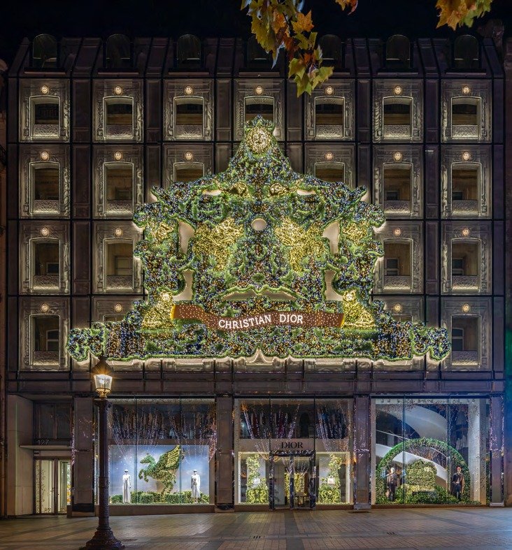 Building facade covered by a large illuminated foliage archway over lit ground-floor windows.