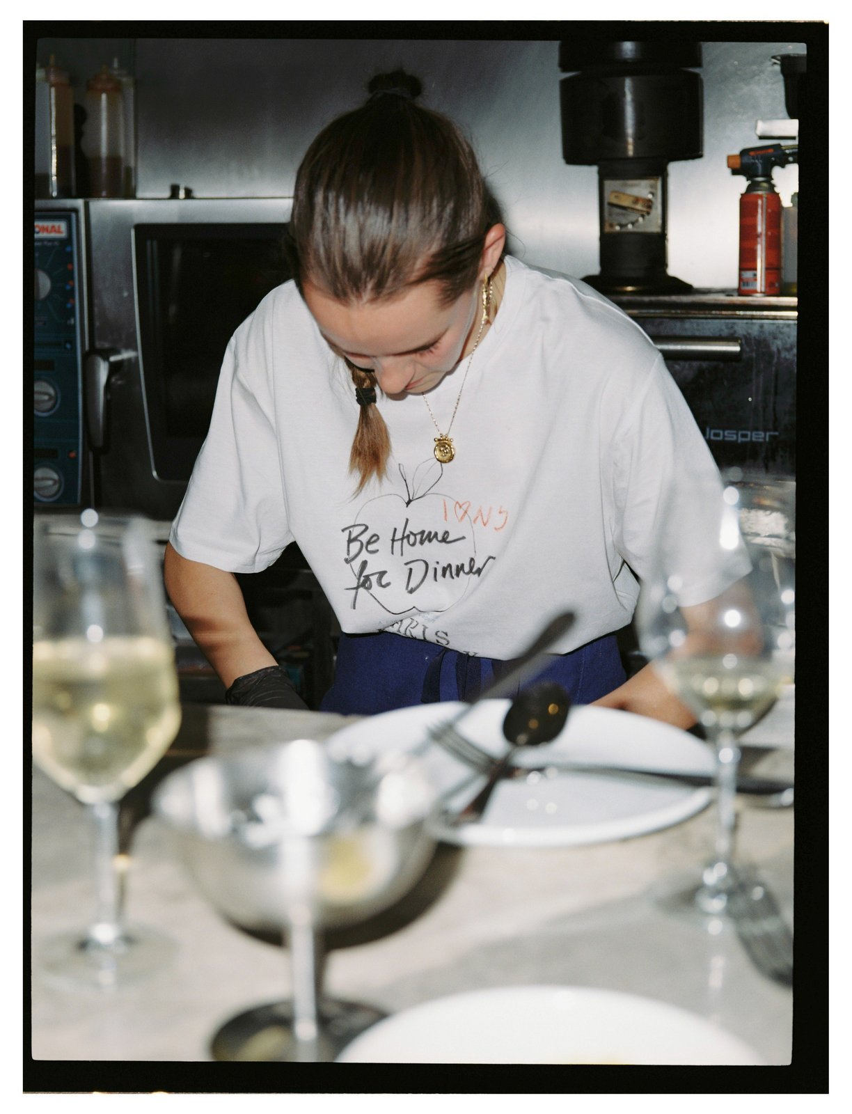 A person with a plaited ponytail in a printed tee works over plates at a counter.