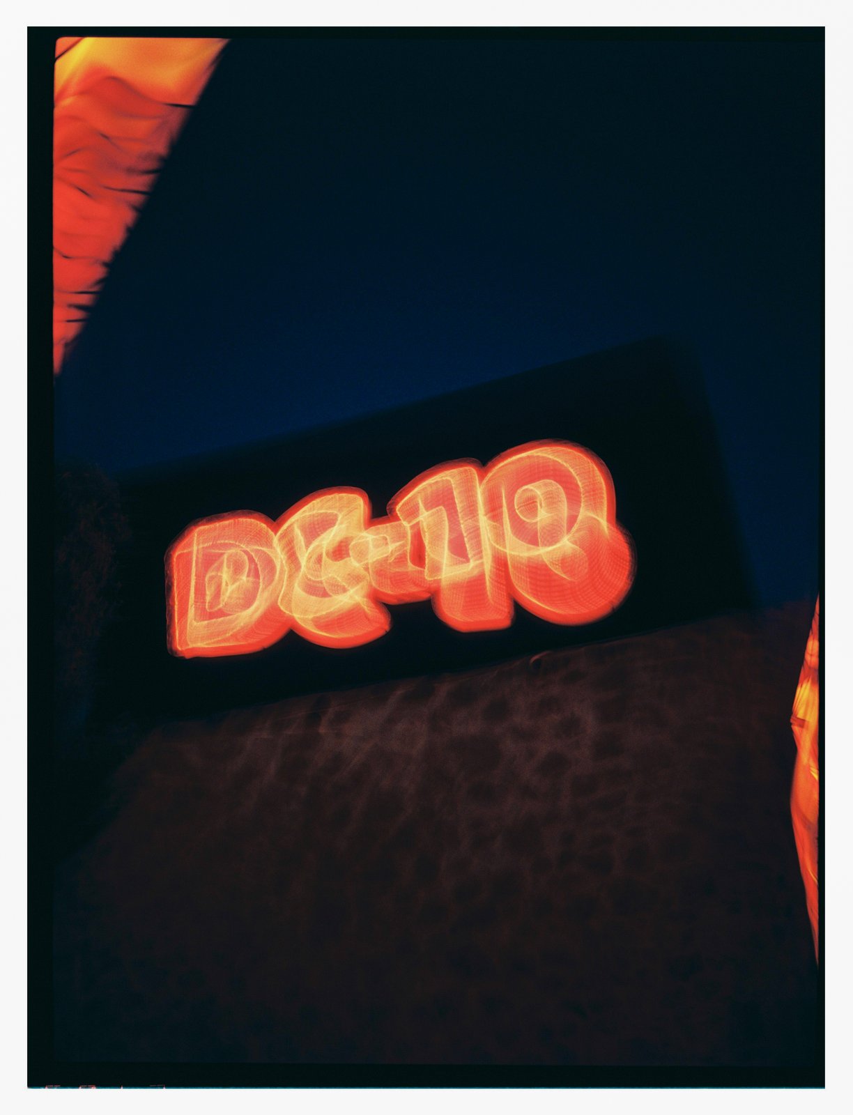 Blurry orange neon signage glowing against a dark night sky, grainy flash-lit film.