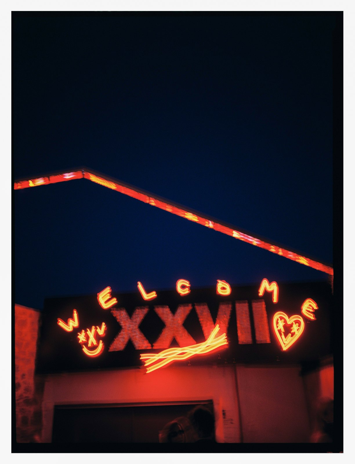Neon signage with a smiley face and heart glowing above a building at night.