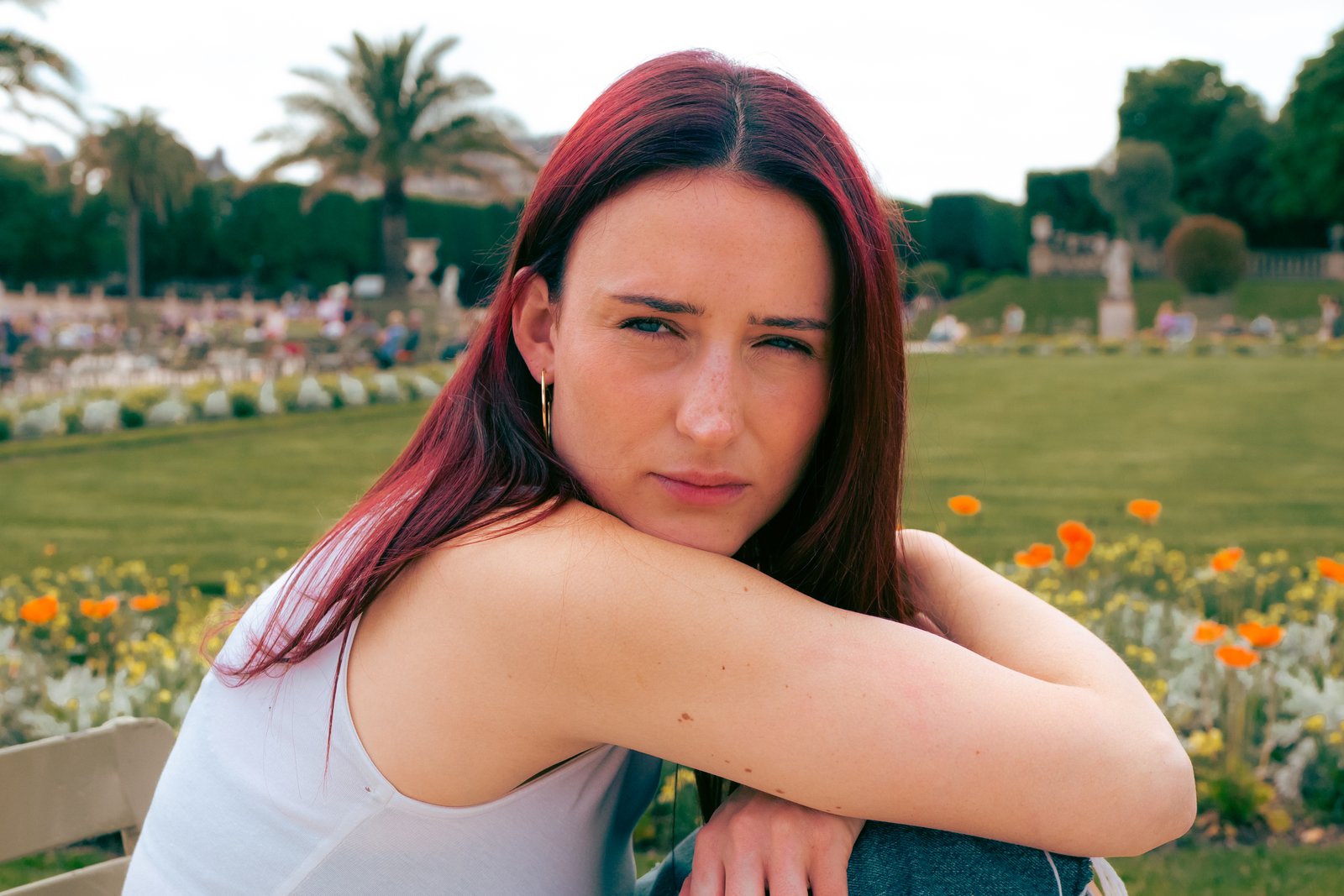 Close portrait of a red-haired woman resting on her arm before a green park with orange flowers.