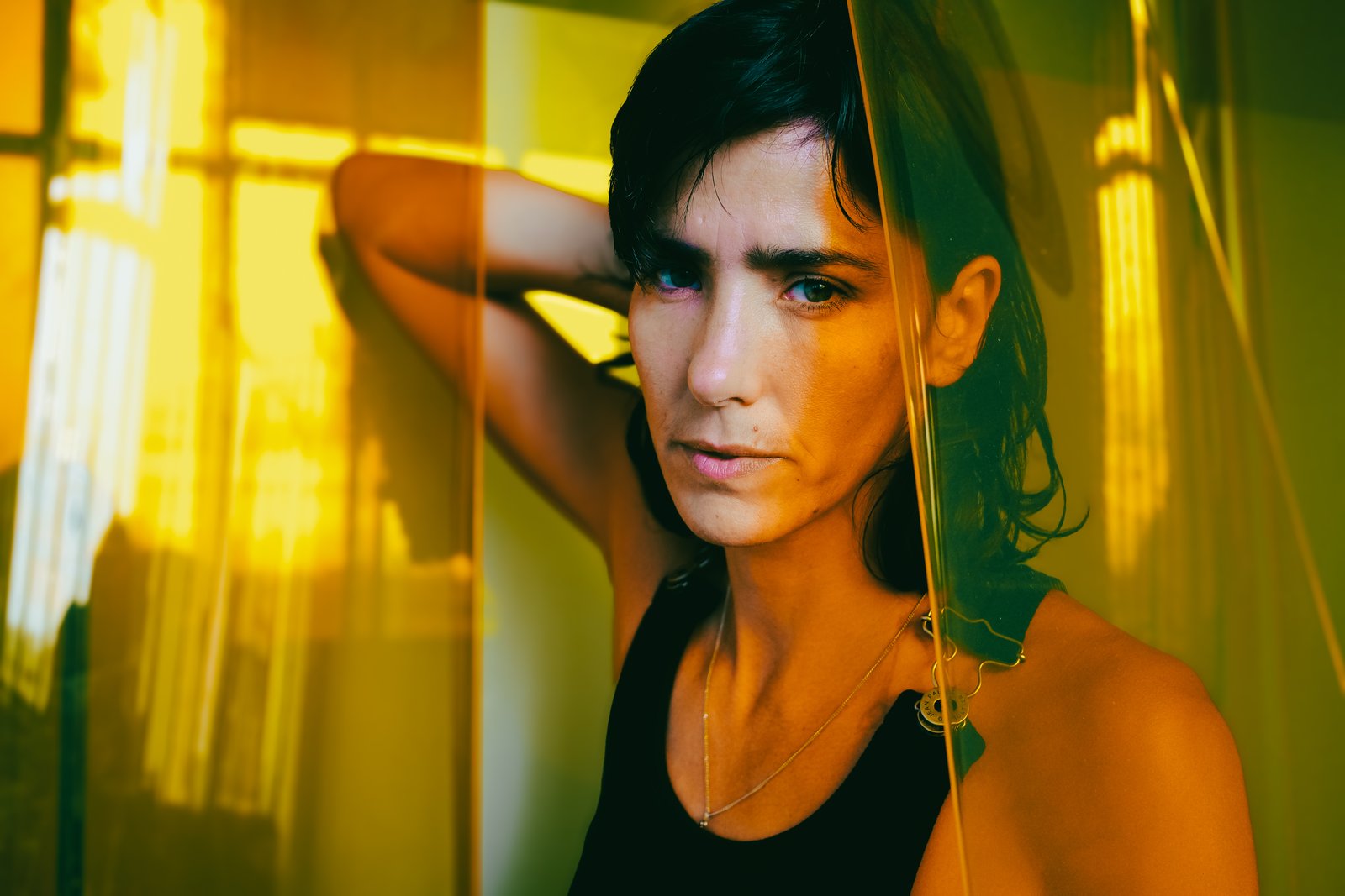 Close portrait of a person with a hand raised to their hair, lit by warm golden light through a window.