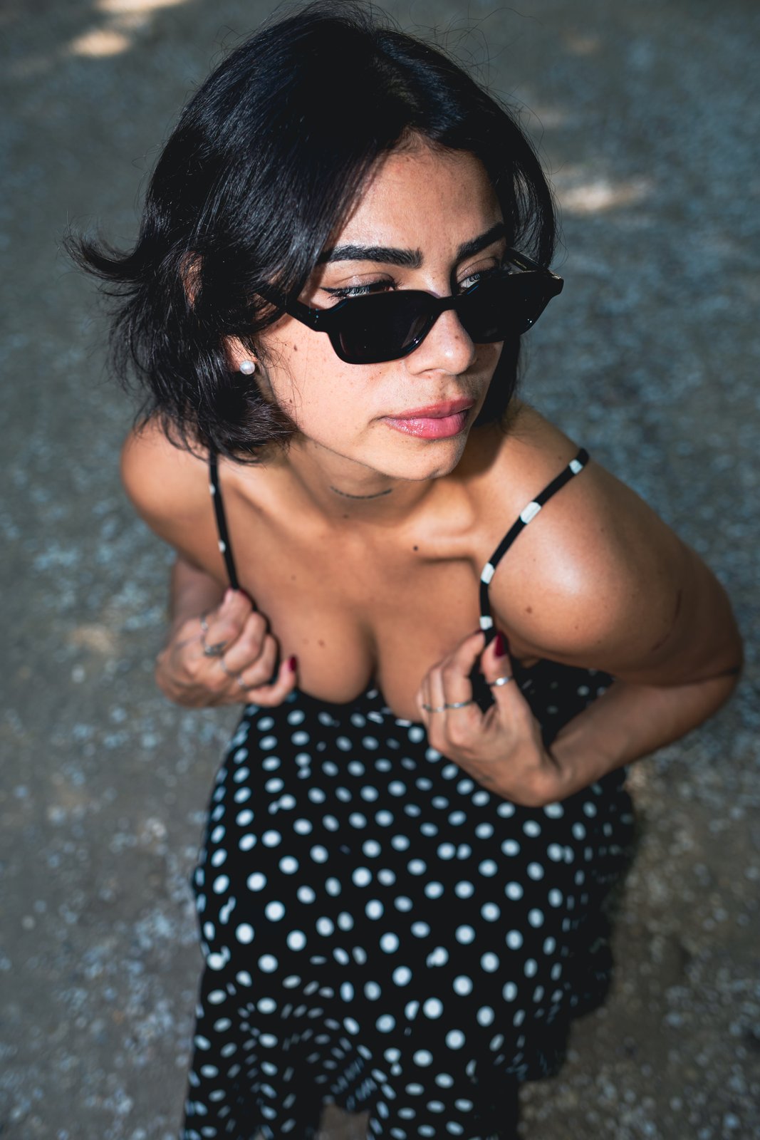 Overhead shot of a woman in sunglasses and a polka-dot dress on sunlit gravel.