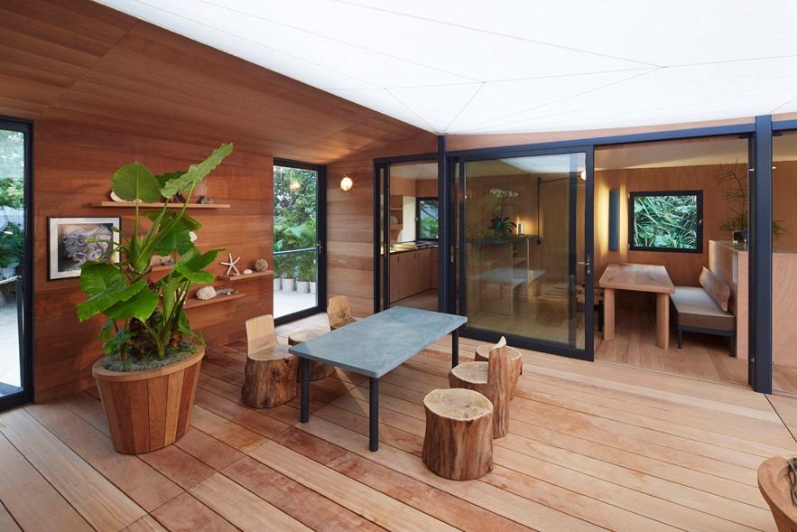 Timber-lined interior with a stone-top table, log stools and a large potted plant.