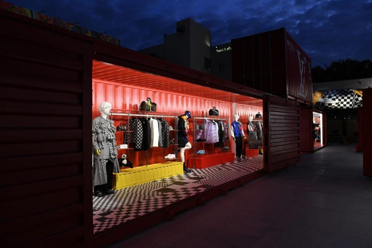 Night view into a red container fitted as a boutique with mannequins and lit shelving.