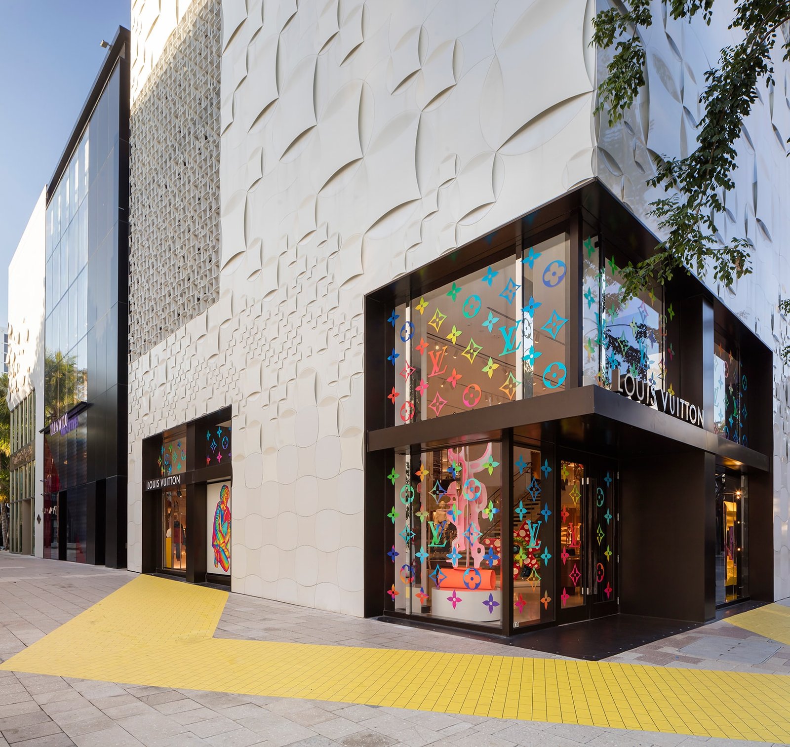 Boutique corner with textured white facade and windows covered in multicoloured monogram flowers.