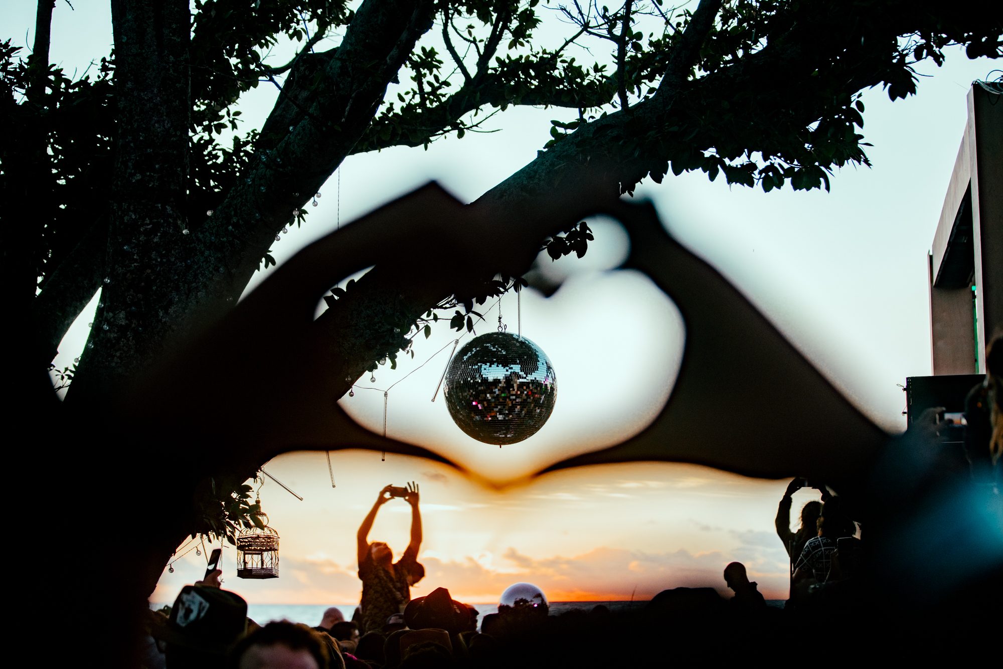 Hands forming a heart shape around a mirrored disco ball glinting in the sunset light.